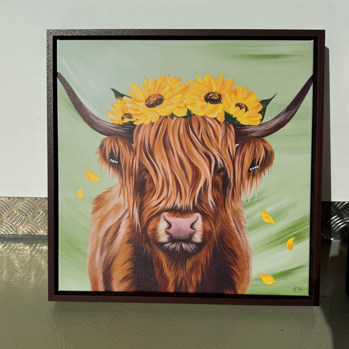A framed painting of a Highland cow with a sunflower crown, displayed against a light gray wall.