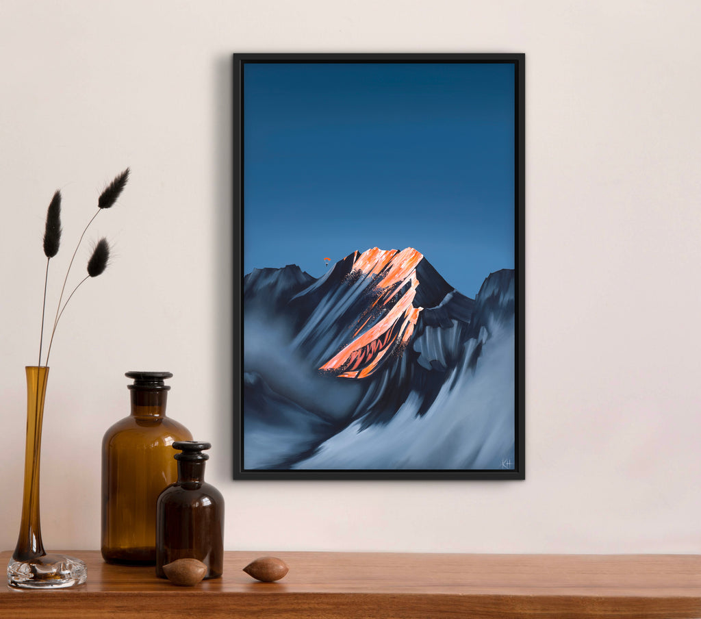 Framed mountain artwork on a wall above a wooden shelf with decorative items.