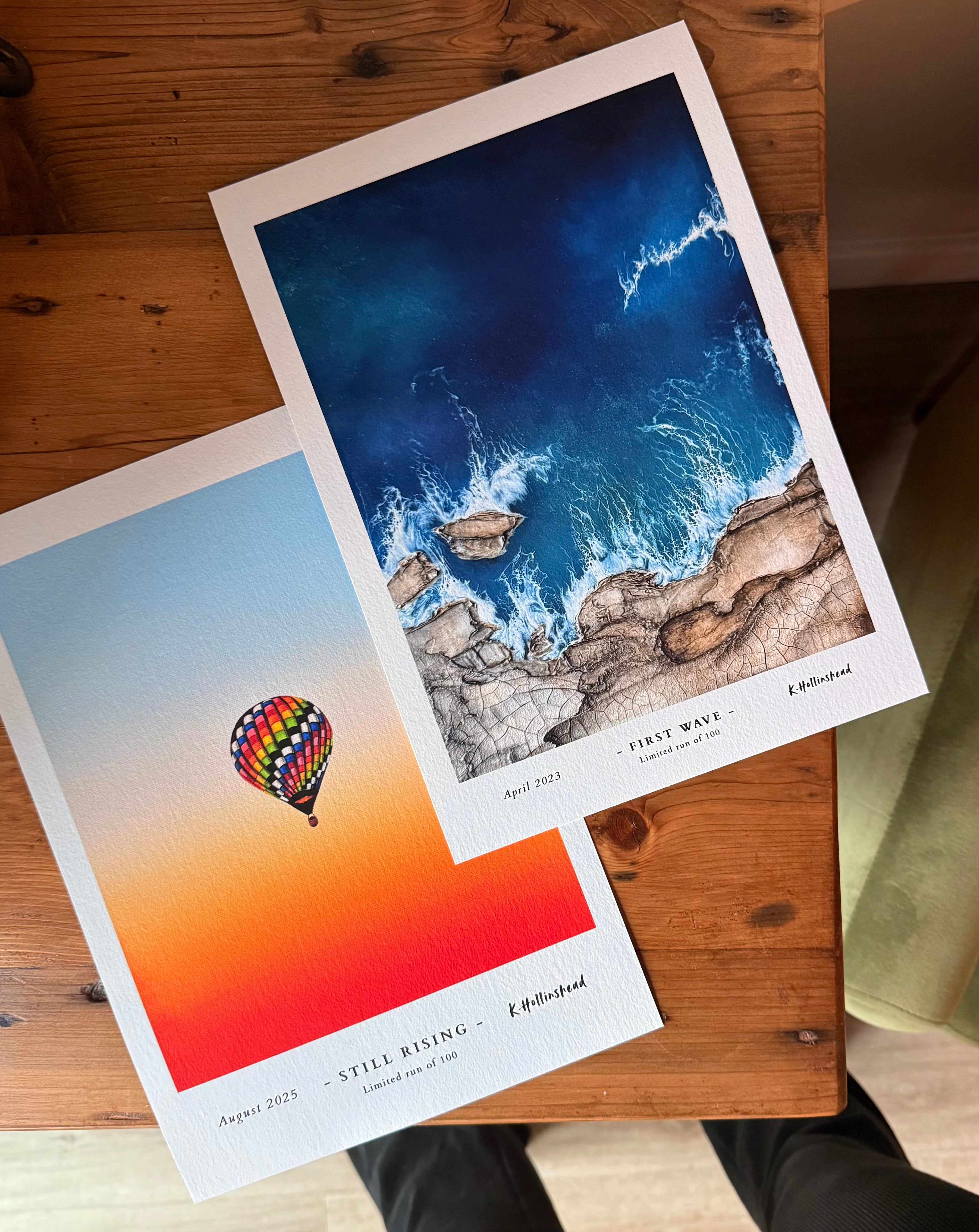 Two prints on a wooden surface, one with a hot air balloon and the other with a mountain and water scene.