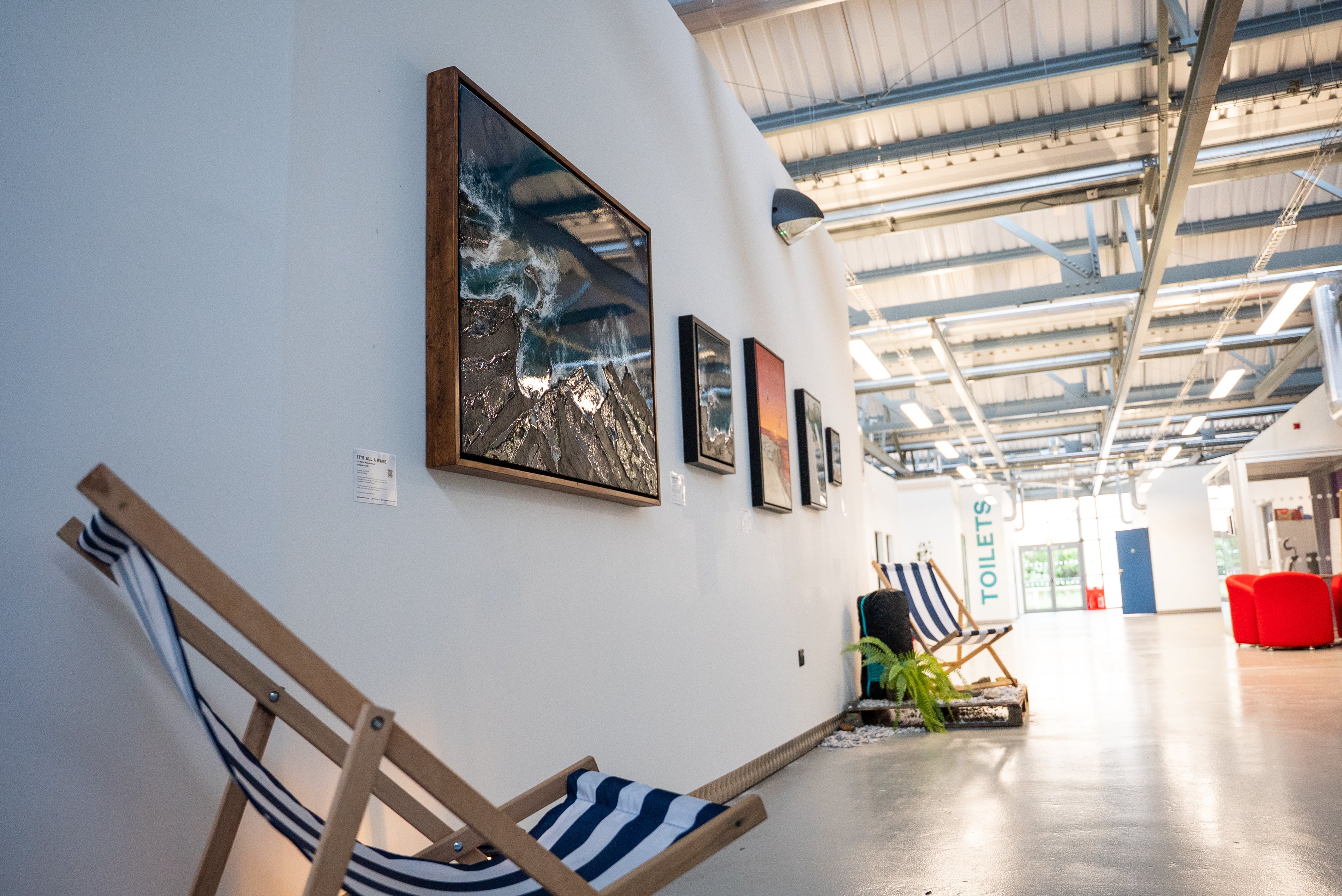 A large framed landscape photograph of a mountain river scene hangs on a white wall in a modern industrial loft space. Art in Hereford