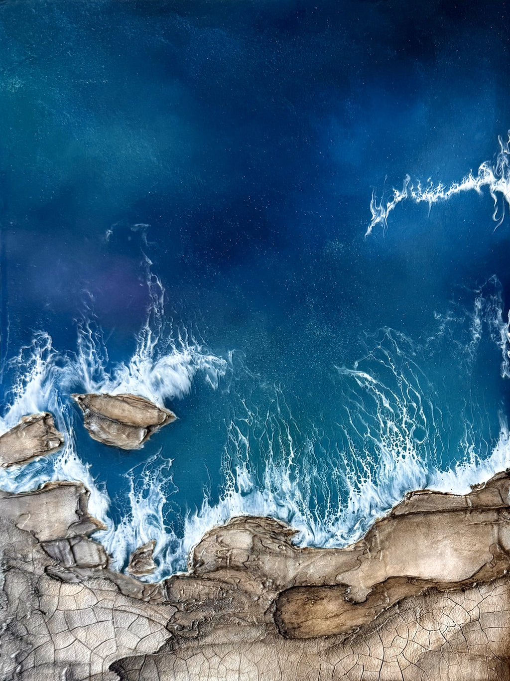 Top-down view of rocky coastline with blue ocean waves.