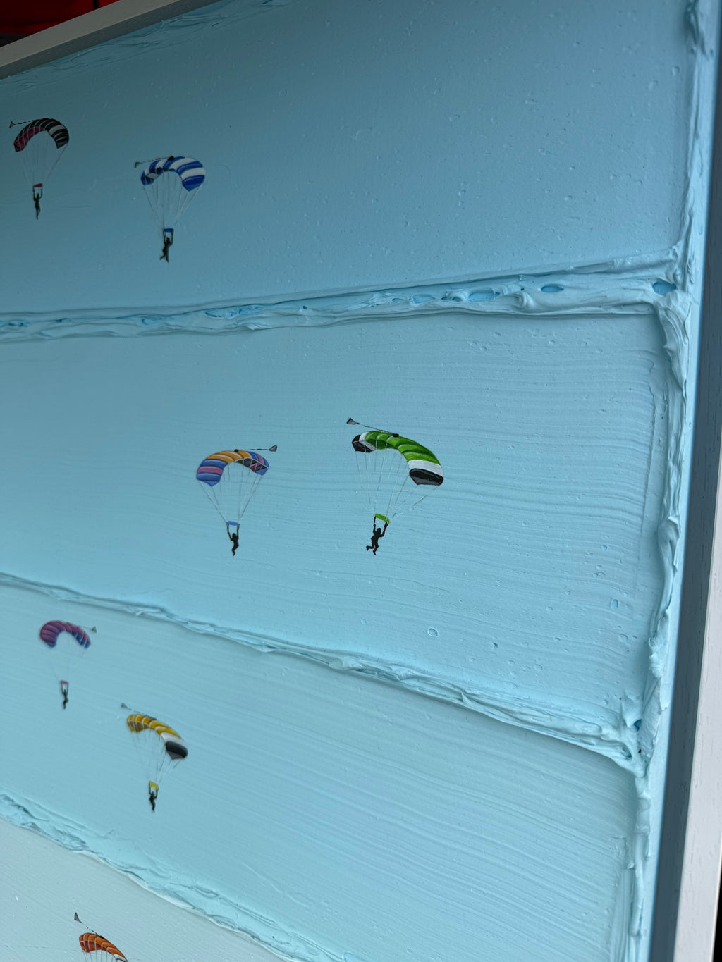 A close-up of a light blue textured surface, likely a canvas print or decorative panel, decorated with small colorful parachute illustrations.