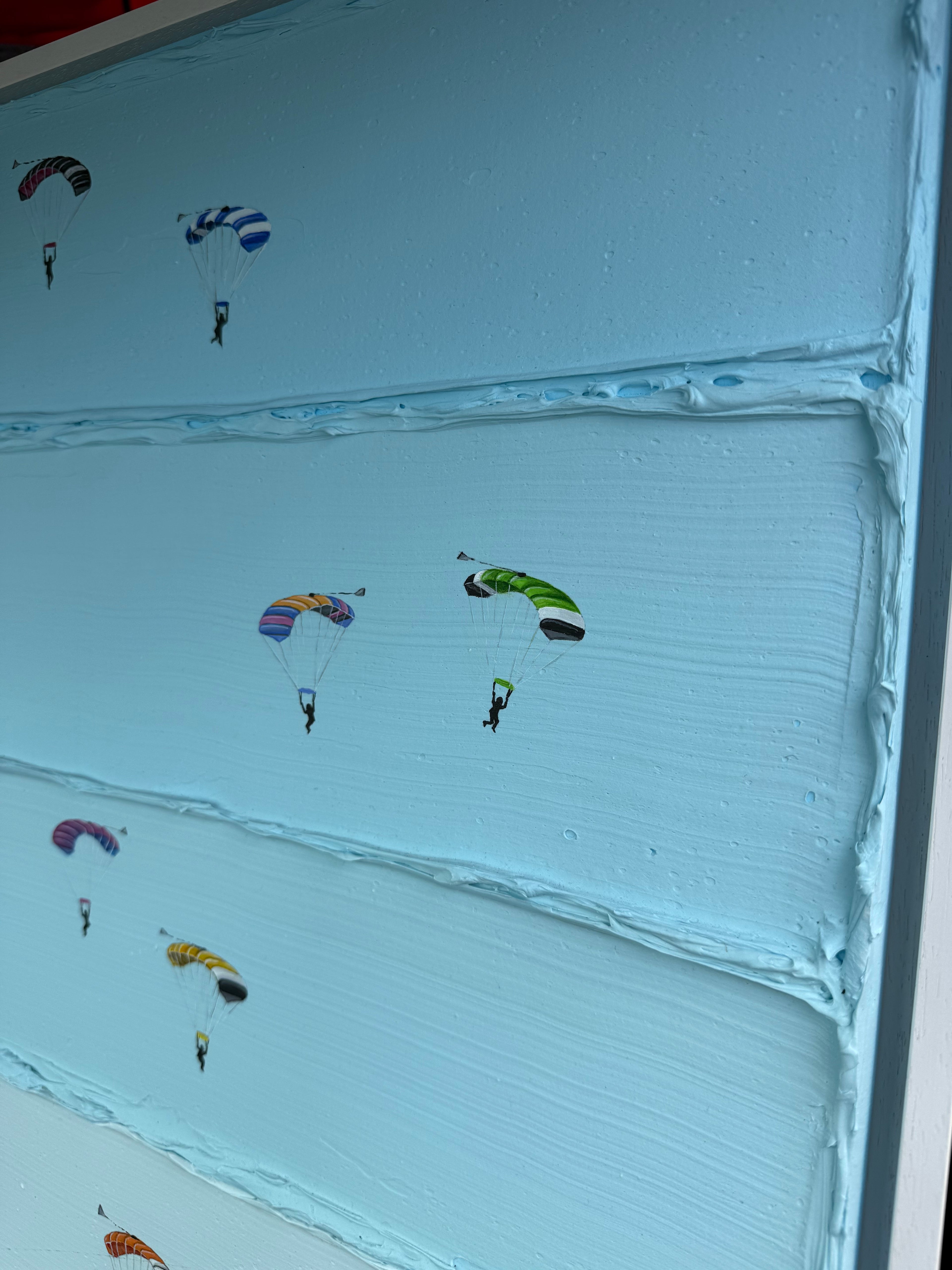 A close-up of a light blue textured surface, likely a canvas print or decorative panel, decorated with small colorful parachute illustrations.