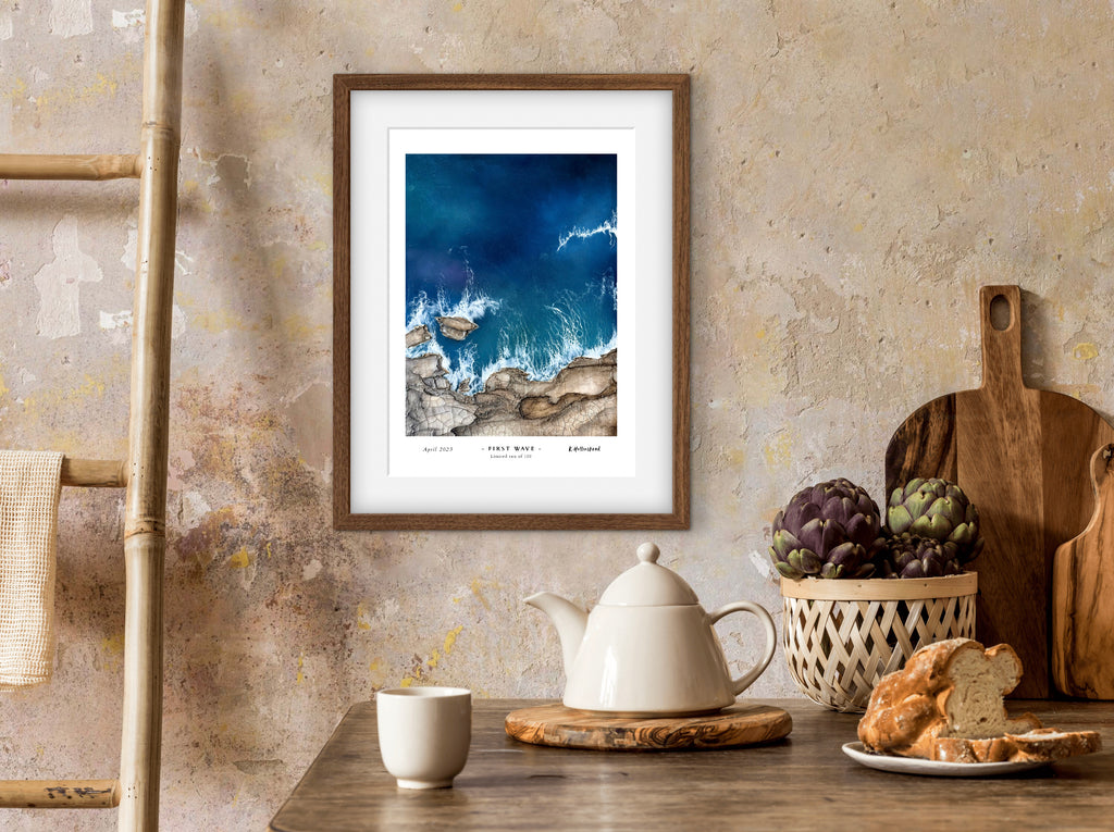 Framed artwork on a wall above a table with a teapot, cups, and bread.