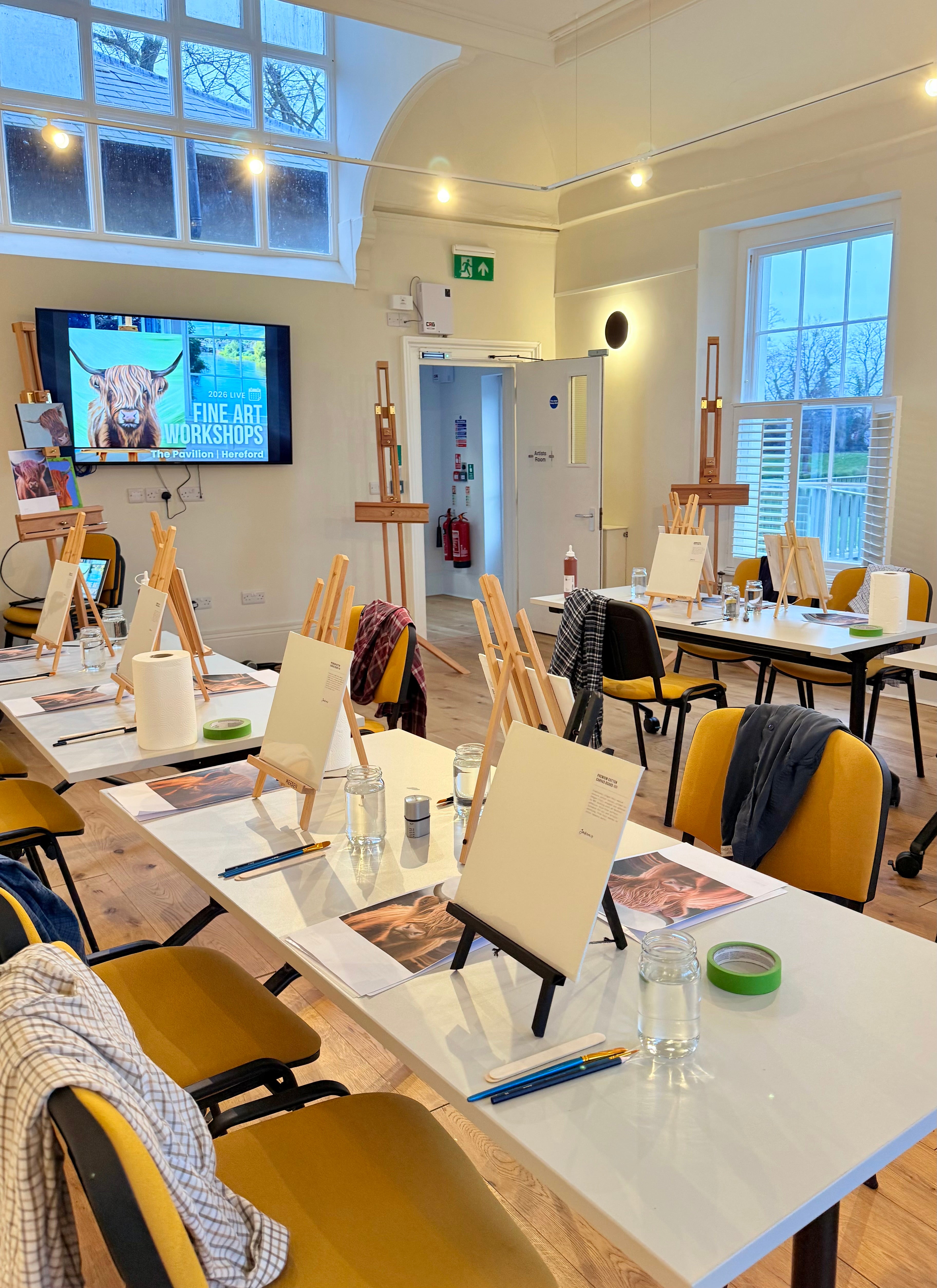 Art studio with tables, easels, and a TV screen displaying an art lesson.