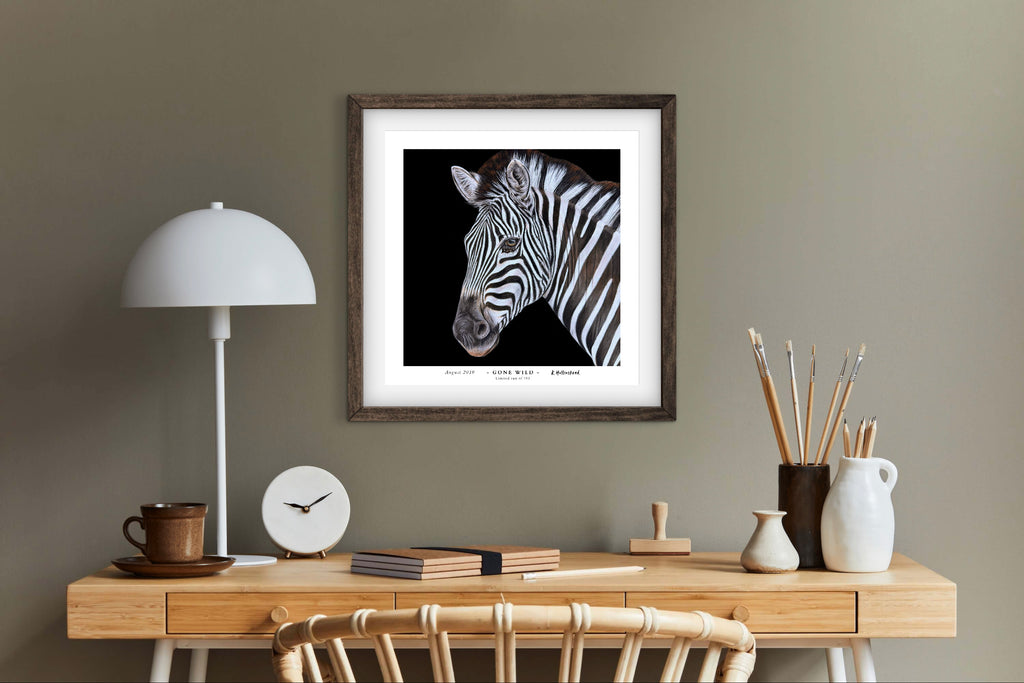 Framed zebra fine art print on a wall above a wooden desk with decor items.