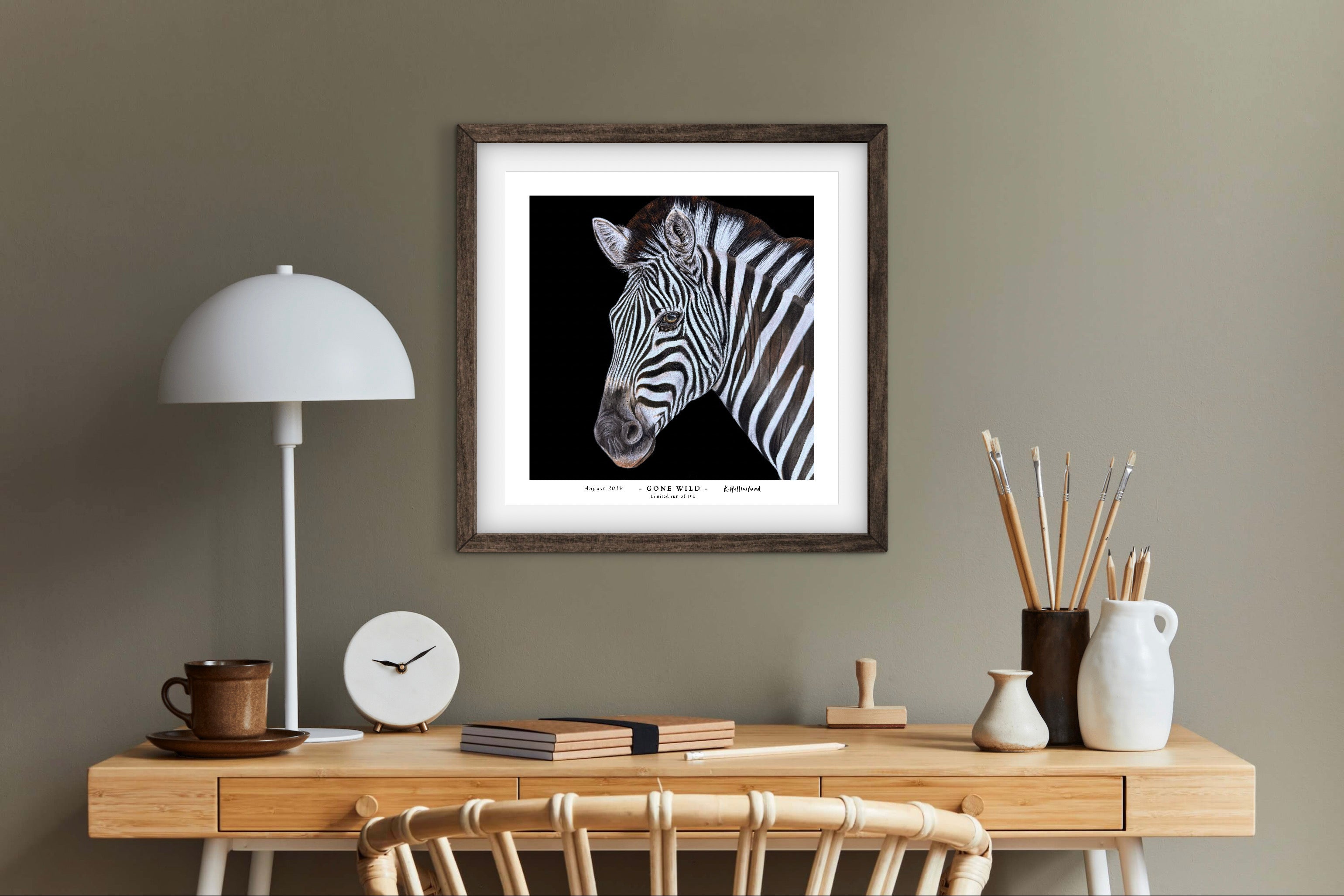 Framed zebra fine art print on a wall above a wooden desk with decor items.