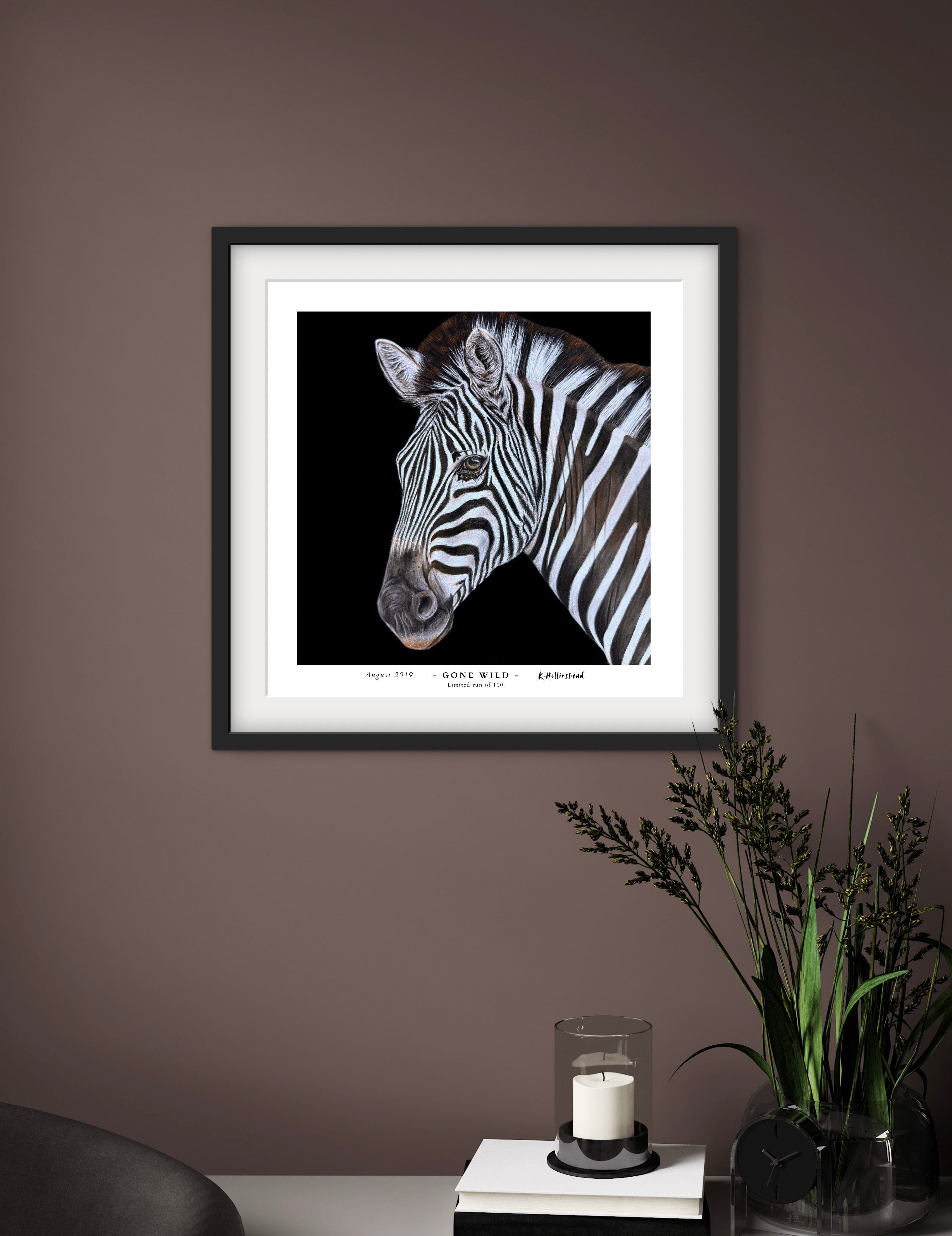 Framed picture of a zebra on a wall with a side table and plant in the foreground.
